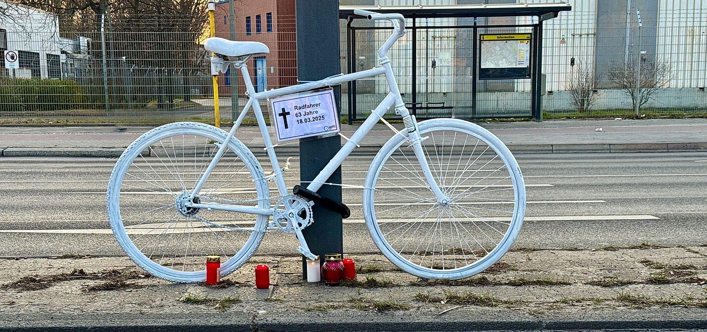 ein weißes Geisterrad mit Informationsschild "Radfahrer 63 Jahre" und Vision Zero Fahne im Vordergrund