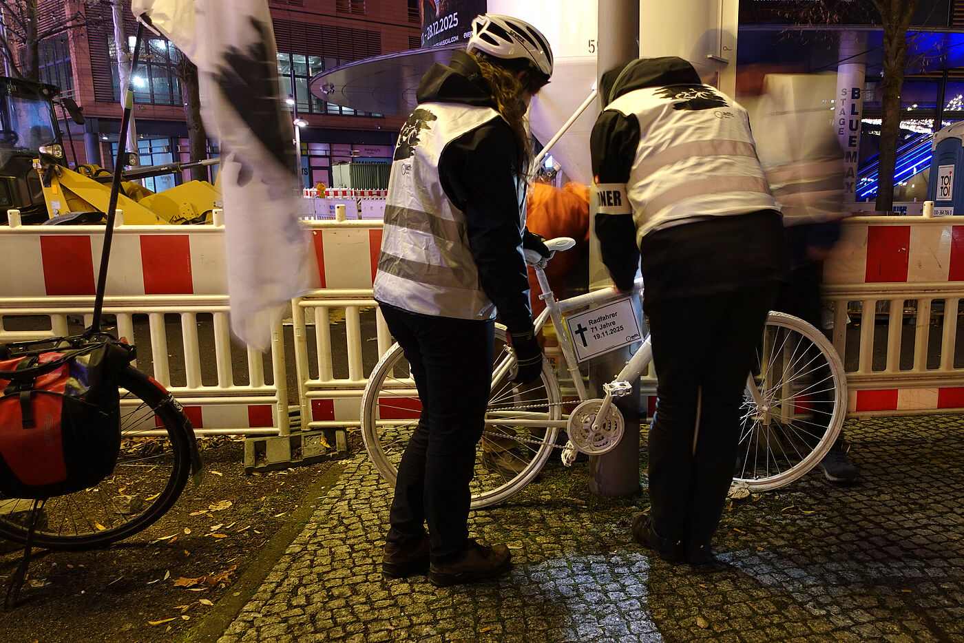 Geisterrad 24.11.2025 Mitte ein weißes Geisterrad wird von Menschen mit weißer Warnweste an einem Laternenpfahl angebracht