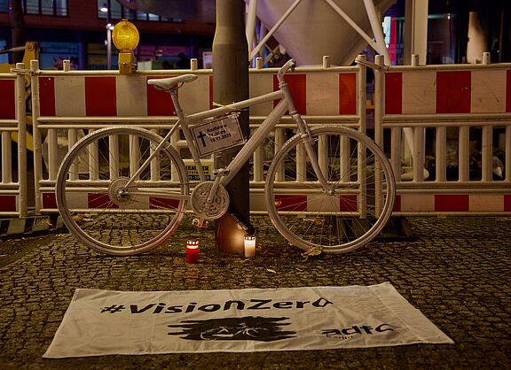 Geisterrad 24.11.2025 Mitte Ein weißes Geisterrad an einem Laternenphal davor eine weiße Vision Zero Fahne