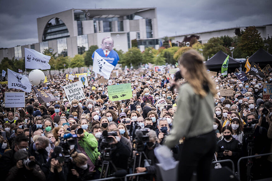 Klimastreik 22.10.21 Eine Bühne mit Sprecherin von hinten, im Hintergrund sind die zuschauenden Menschen vor der Bühne zu sehen.