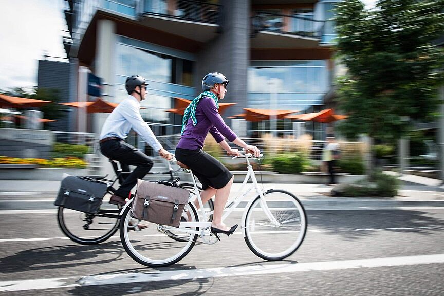 NRW will Pendelverkehr in Radverkehr wandeln. Zwei Menschen fahren nebeneinander Fahrrad in einem städtischen Umfeld.